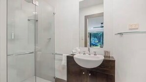 Et moderne badeværelse med brusekabine i glas, et hvidt håndvaskarrangement og en mørk trækommode.