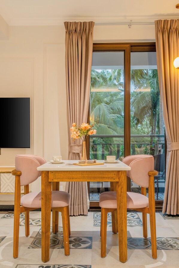Un comedor con mesa de madera y sillas rosas, un jarrón con flores y vistas a palmeras a través de un ventanal.