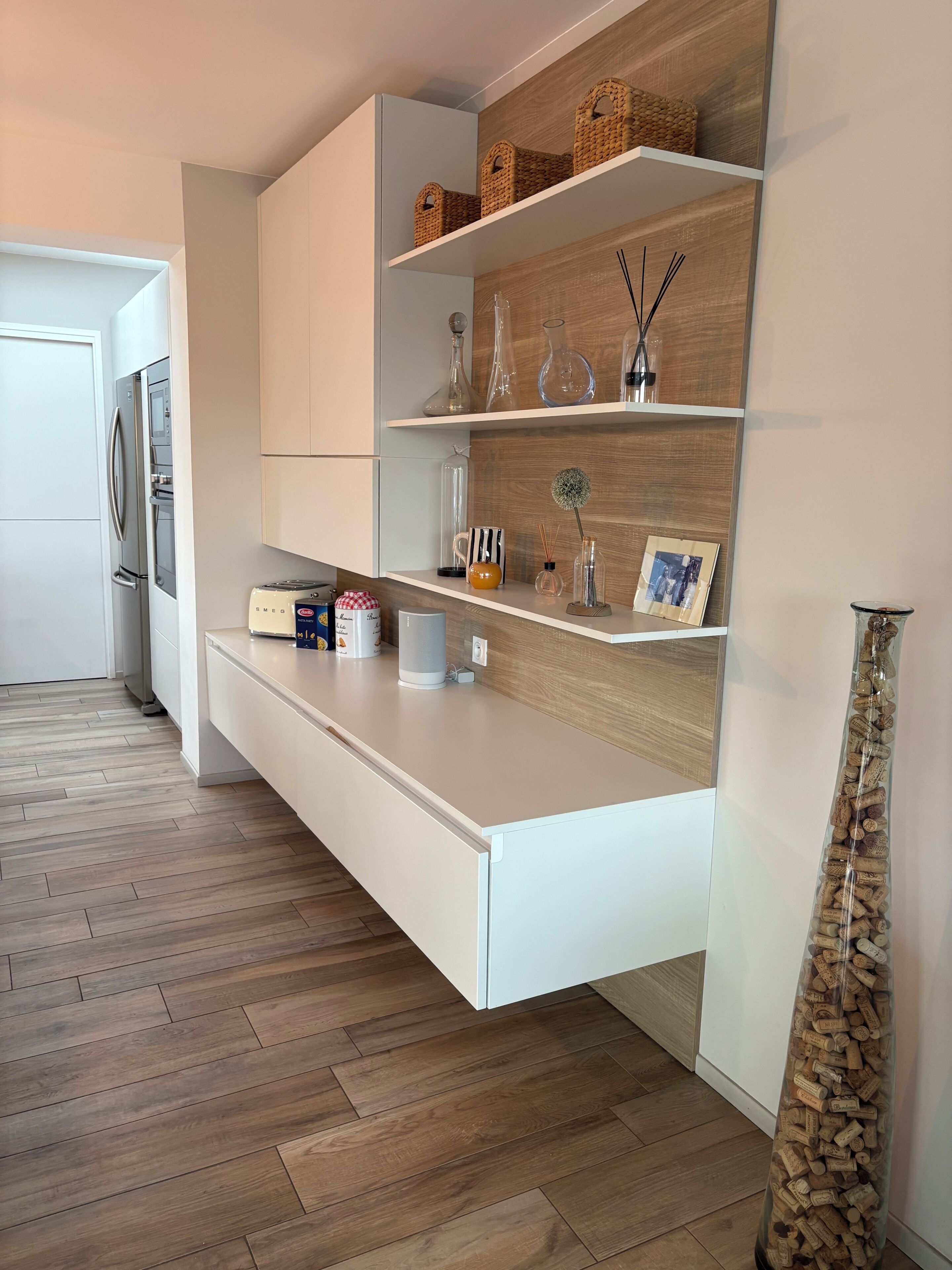 A modern kitchen with white cabinetry, wooden flooring, and a built-in shelf unit with decorative items.