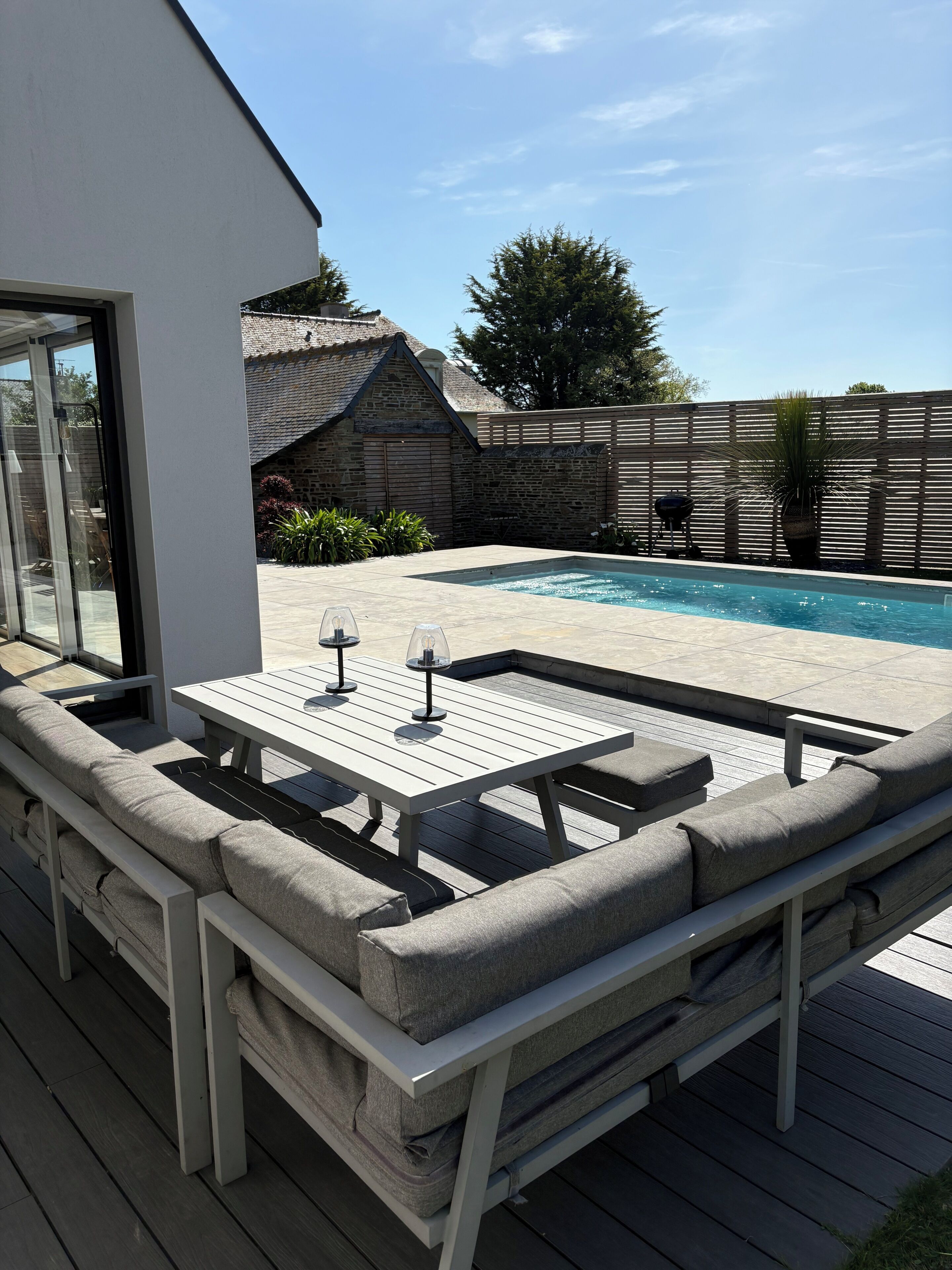 Een zwembadterras met een ingebouwde bank en tafel, omgeven door een houten terras en een stenen muur.
