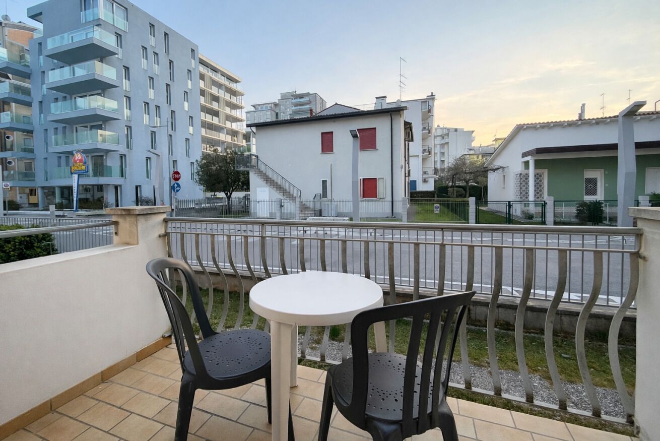 A balcony with two chairs and a small table, overlooking a street with buildings and a staircase.