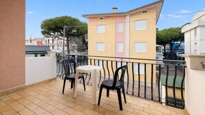 A balcony with two chairs and a table, a yellow building in the background, and a clear sky. - Villa Luisa 2 - Carraro Immobiliare Jesolo (Lido di Jesolo)