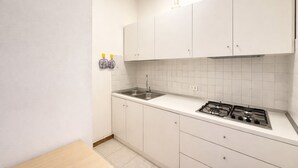 A small kitchen with white cabinets, a sink, and a gas stove. - Villa Luisa 2 - Carraro Immobiliare Jesolo (Lido di Jesolo)