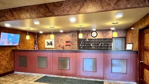 A reception area with a marble wall, a reception desk with glass panels, a clock, and a television mounted on the wall. - Lenox Hotel and Suites (Buffalo)