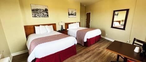 A hotel room with two beds, a wooden floor, a dining table with chairs, and a mirror on the wall.