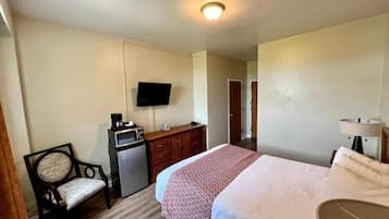 A hotel room with a bed, a desk with a microwave, a chair, a television, and a lamp.