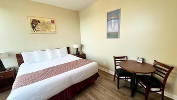Una habitación de hotel con una cama grande, una mesita pequeña, dos sillas, una mesita de noche y dos cuadros colgados en la pared.