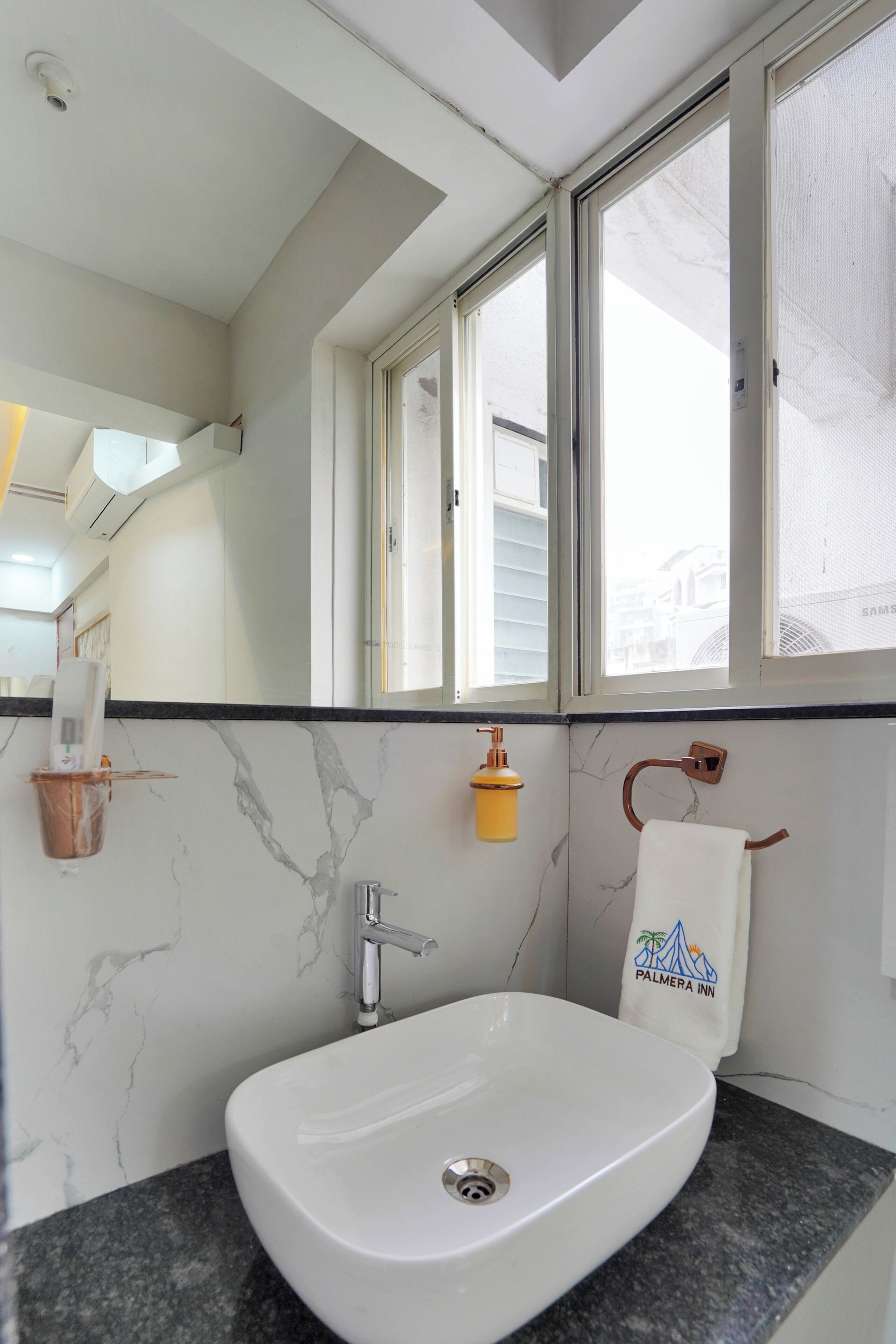 A bathroom with a white sink, a towel rack with a towel, a small yellow soap dispenser, and a window above the sink.