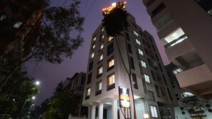 Un edificio a più piani con insegne illuminate, un ingresso carrabile e una strada con auto parcheggiate e alberi.