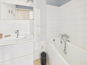 Une salle de bain avec un lavabo blanc, un miroir et une baignoire.