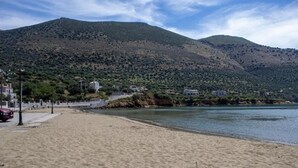 Een strand met een berg op de achtergrond, een verharde promenade en gebouwen aan de kust.