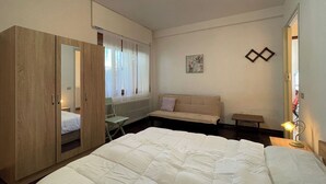 A bedroom with a large bed, a wardrobe, a sofa, a small table, and a mirror.
