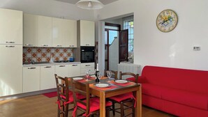 A dining area with a table set for four, a red sofa, and a kitchen with white cabinets and a red-tiled backsplash.