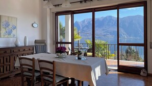 A dining area with a table set for two, a wooden cabinet, and a view of mountains through large windows.