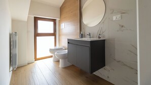 A modern bathroom with a wooden vanity, a round mirror, and a toilet.