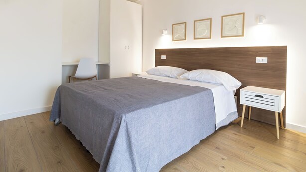 A bedroom with a bed, bedside table, chair, and wall-mounted lights.