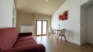 A living room with a red sofa, a dining area with a table and chairs, and a door leading to another room.