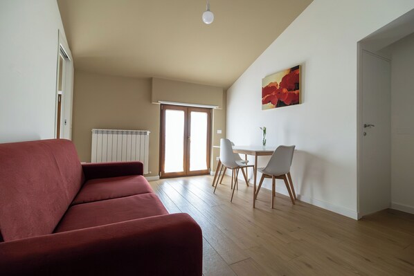 A living room with a red sofa, a dining area with a table and chairs, and a door leading to another room.