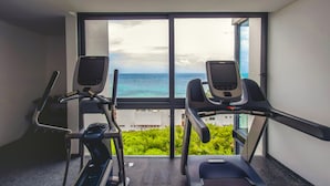 Ett gym med två löpband och en motionscykel, med utsikt över ett vackert landskap med havet och grönområden.