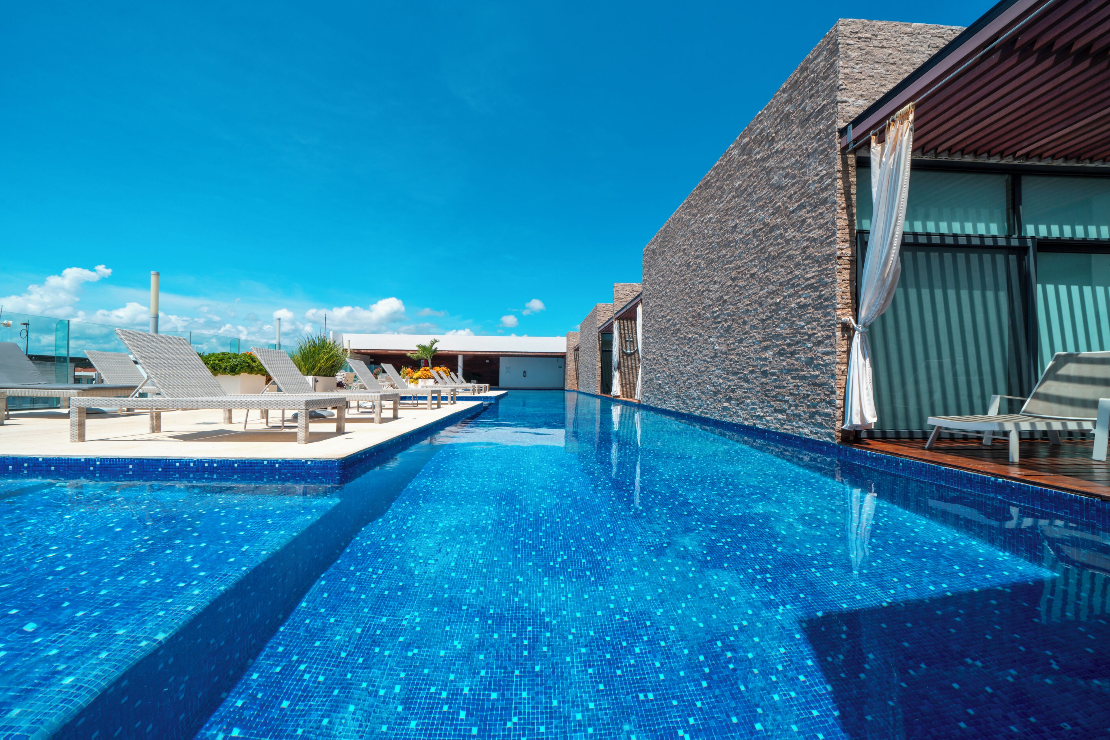 A swimming pool with clear blue water, lounge chairs, and a stone building with large windows.