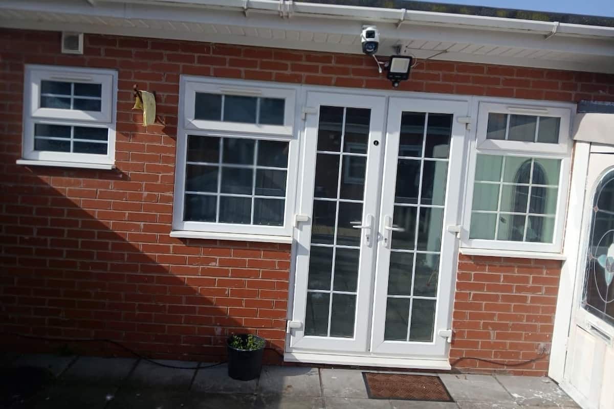 A brick house with a white front door, two windows, and a security camera.