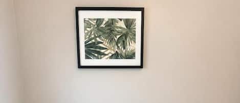 A neatly made bed with a white comforter and pillows, a framed picture above the bed, and a bedside lamp on the right.