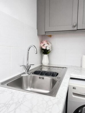 A kitchen with a stainless steel sink, a dish drying rack, and a white vase with flowers. - RS Prime Homestay  (Solihull)
