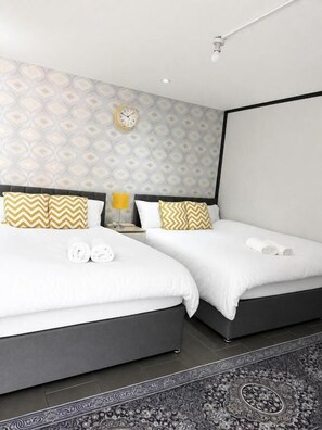 A hotel room with two beds, a patterned wall, a clock, and a rug. - RS Prime Homestay  (Solihull)