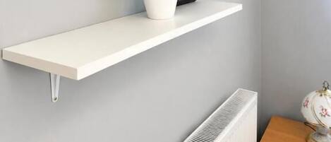 A modern room with a mounted TV, a white shelf with a plant, and a radiator.