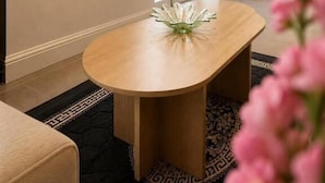 A modern interior with a round wooden table, a vase with flowers, and a patterned rug. - RS Prime Homestay (Solihull)