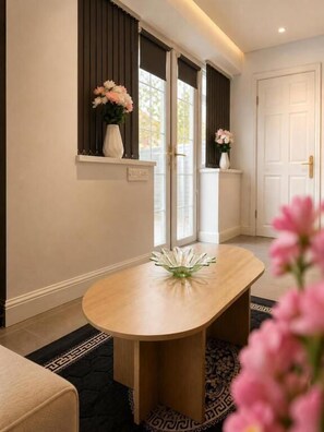 A room with a round wooden table, a vase with flowers, and a window with blinds. - RS Prime Homestay  (Solihull)