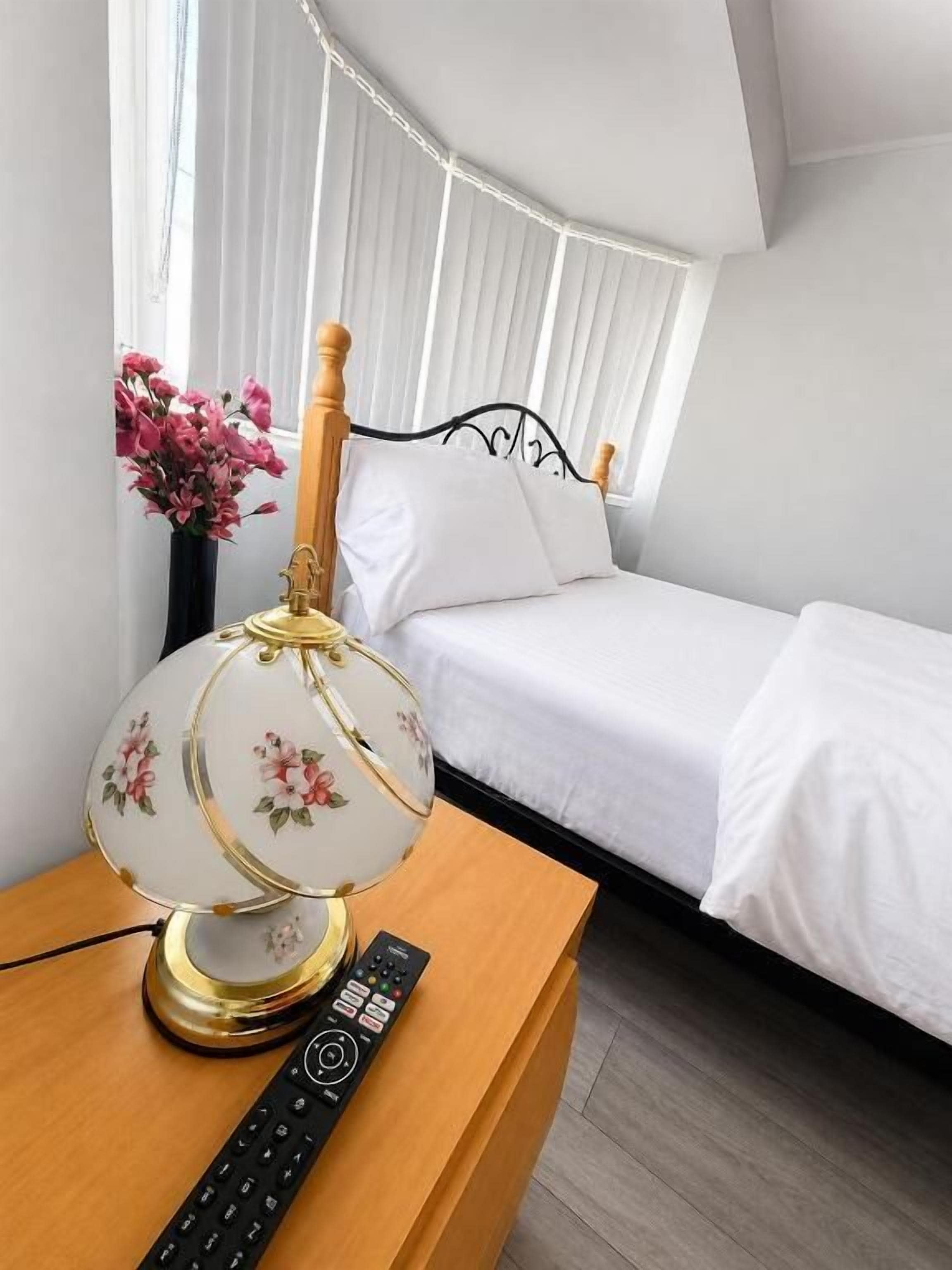 Un dormitorio con una cama, una mesita de noche con una lámpara y un control remoto.