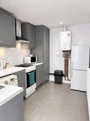 A modern kitchen with grey cabinets, a white refrigerator, a microwave, a stove, and a water heater. - RS Prime Homestay  (Solihull)