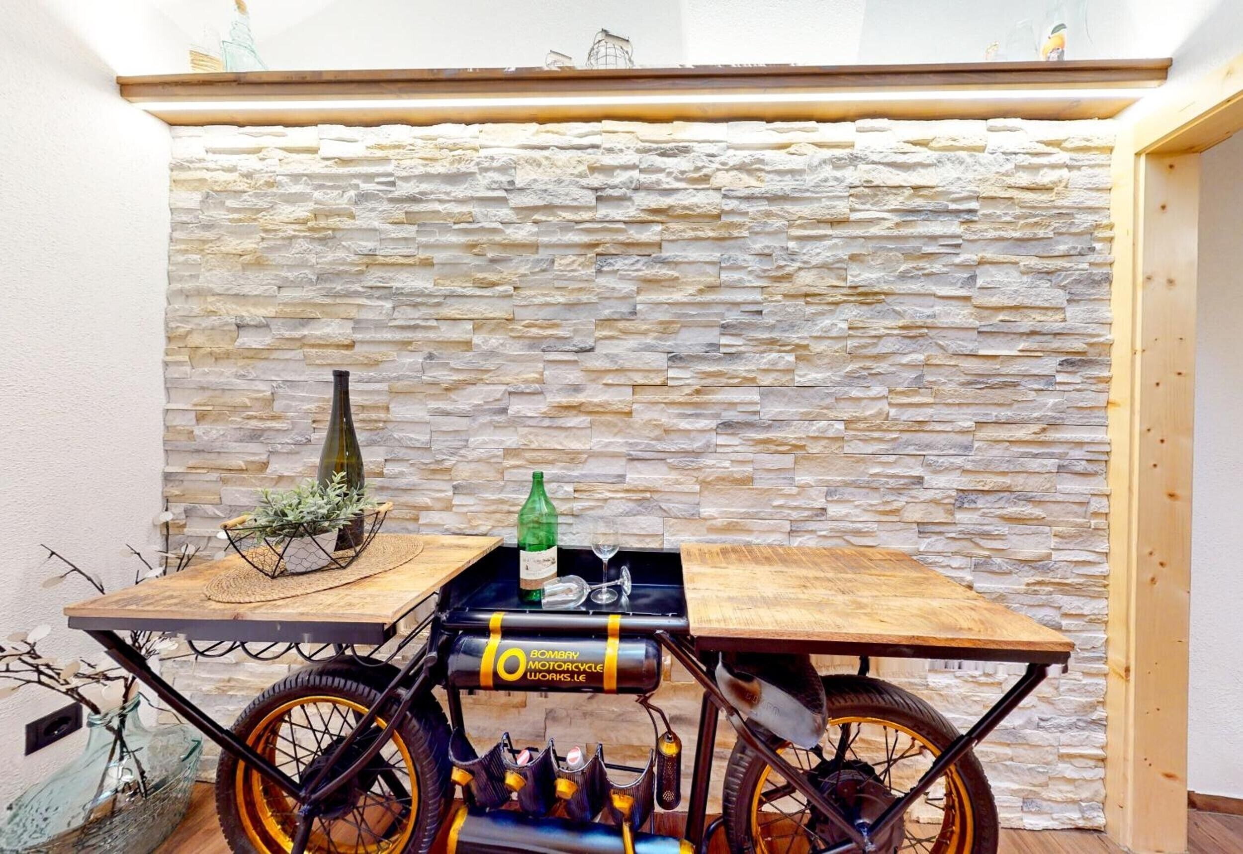 Een kamer met een stenen muur, een houten tafel, een fietskar en een fles.