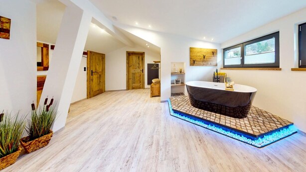Ein modernes Badezimmer mit einer freistehenden Badewanne, Holzboden und gefliestem Bereich um die Wanne.