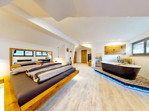 Ein modernes Schlafzimmer mit einem großen Bett, einem integrierten Schreibtisch und einem Badezimmer mit Badewanne.