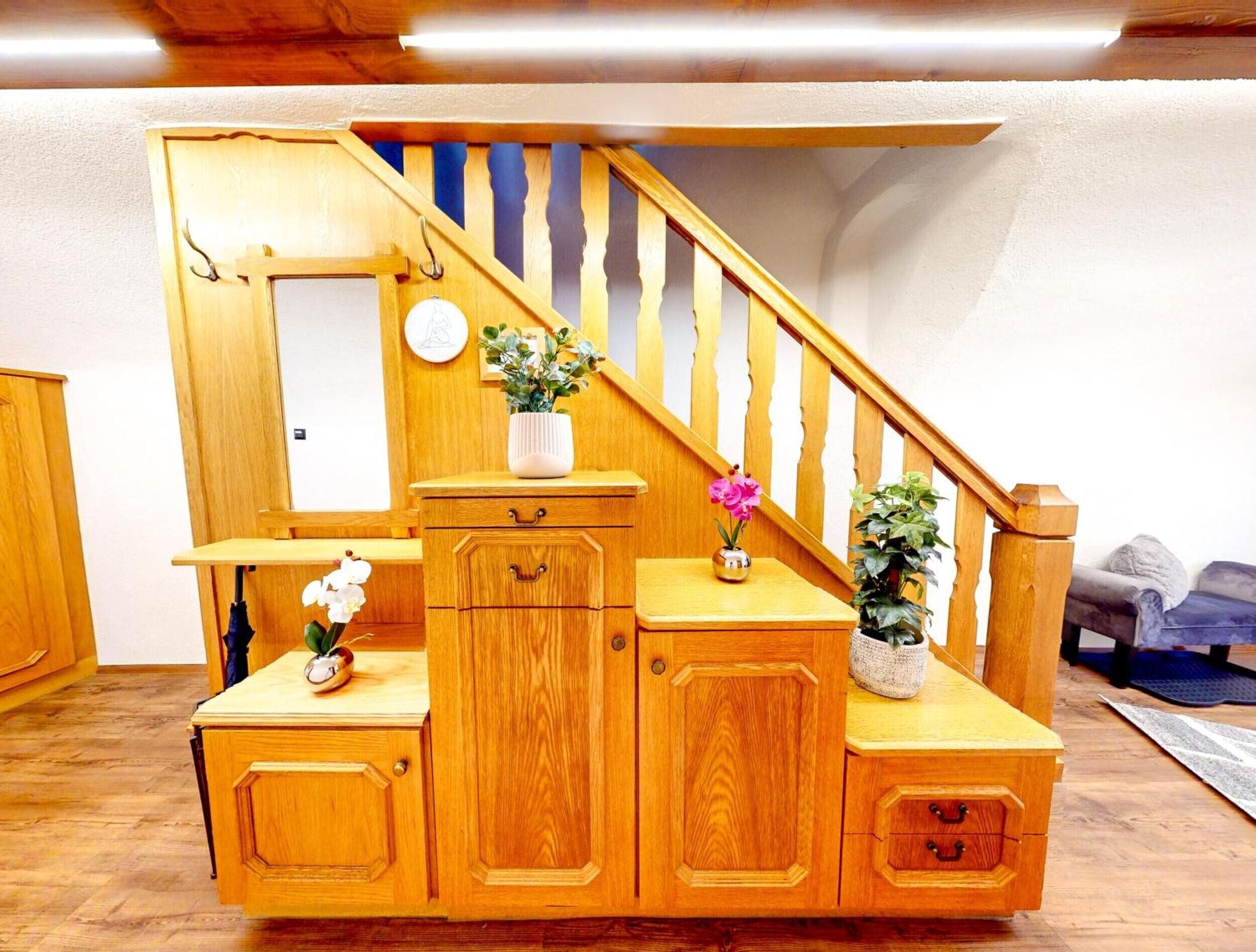 A wooden staircase with a handrail, a small table with a vase of flowers, and a cabinet with drawers.