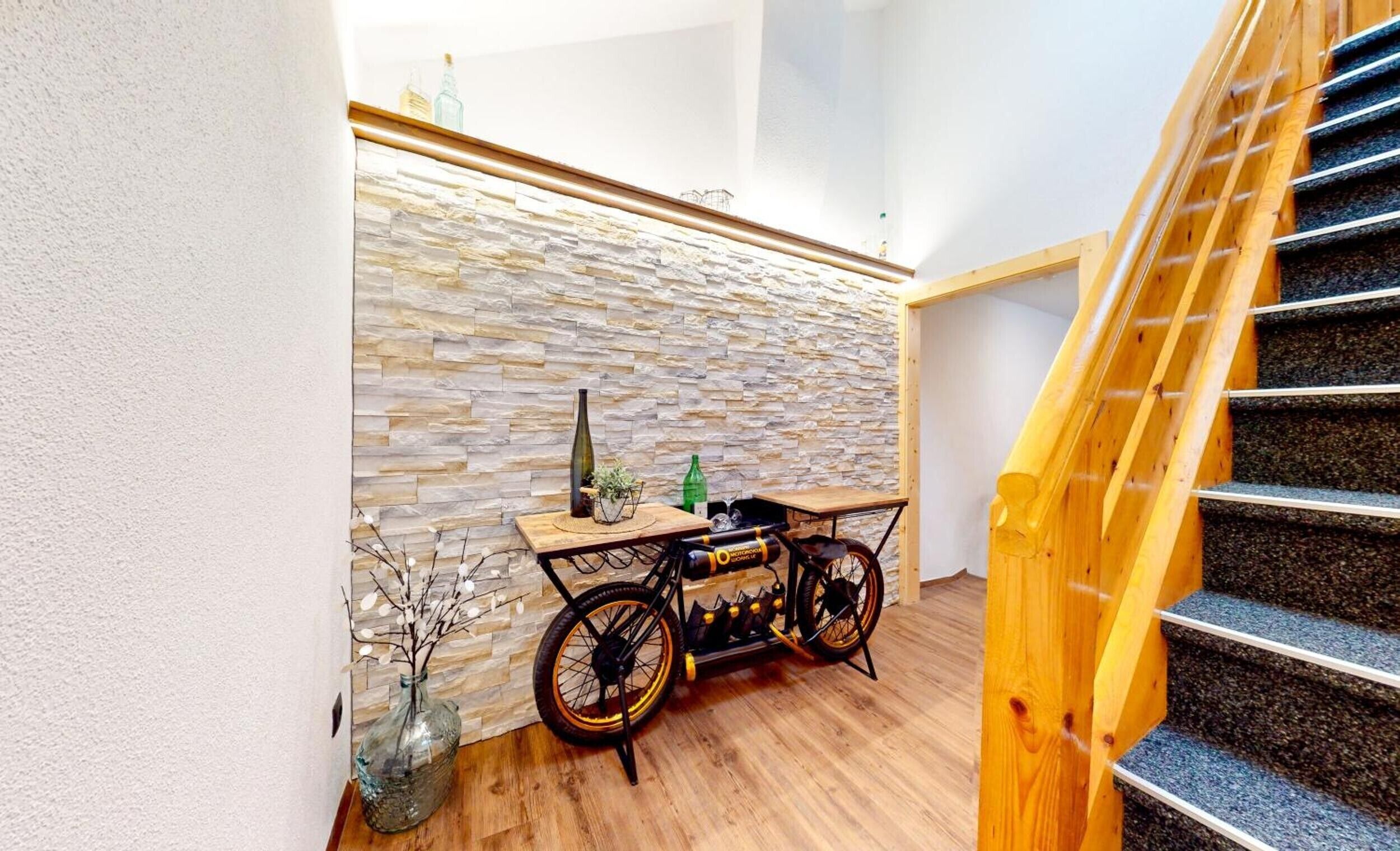 A staircase with wooden steps and a handrail, a stone wall, and a table with a bicycle and various items.