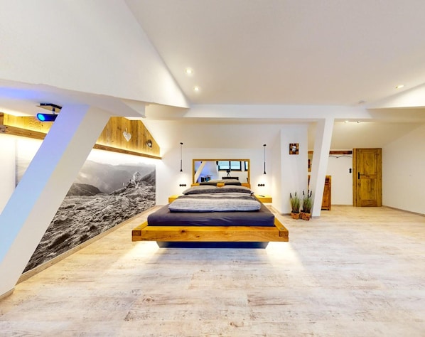 Ein modernes Schlafzimmer mit einem zentral platzierten Bett, einer Holzbalkendecke und einem großen Wandbild.