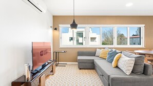 Un salon moderne avec un canapé, un téléviseur et de grandes fenêtres.