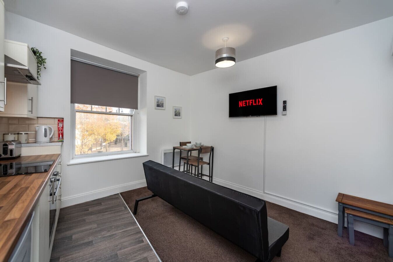 A modern kitchen with a dining area, a bench, and a TV displaying 'NETFLIX'.