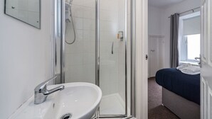 Bany d'hotel amb boxa de dutxa de vidre, un lavabo i un llit amb llençol blau.