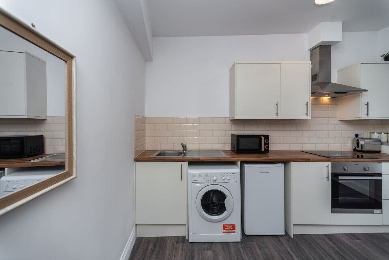 A compact kitchen with a washing machine, microwave, oven, and a sink.