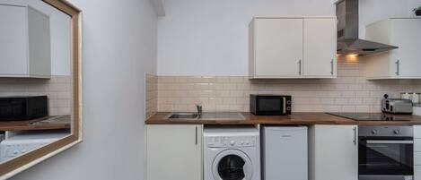 A compact kitchen with a washing machine, microwave, oven, and a sink.