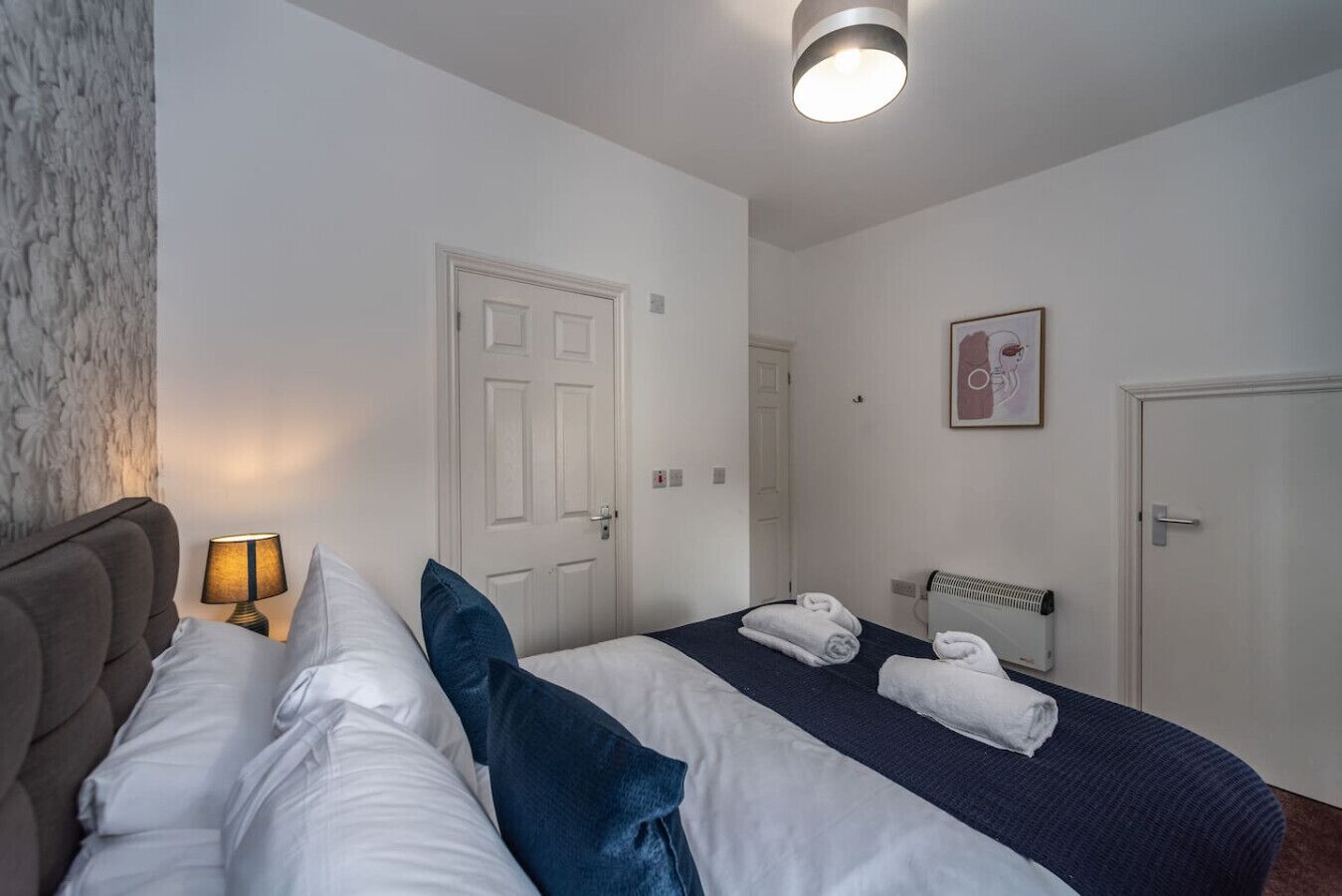 A hotel room with a bed, a bedside lamp, a radiator, and a door.
