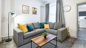 Una sala de estar moderna con un sofá seccional gris, una mesa de centro de madera, una lámpara de pie y un reloj en la pared.