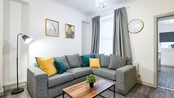 A modern living room with a grey sectional sofa, a wooden coffee table, a floor lamp, and a clock on the wall.