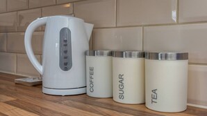 Un bollitore elettrico bianco con display digitale e tre contenitori bianchi etichettati 'COFFEE', 'SUGAR' e 'TEA' su un ripiano di legno.