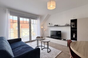 Un salon moderne comprenant un canapé, une petite table, un téléviseur et un coin cuisine avec une étagère.