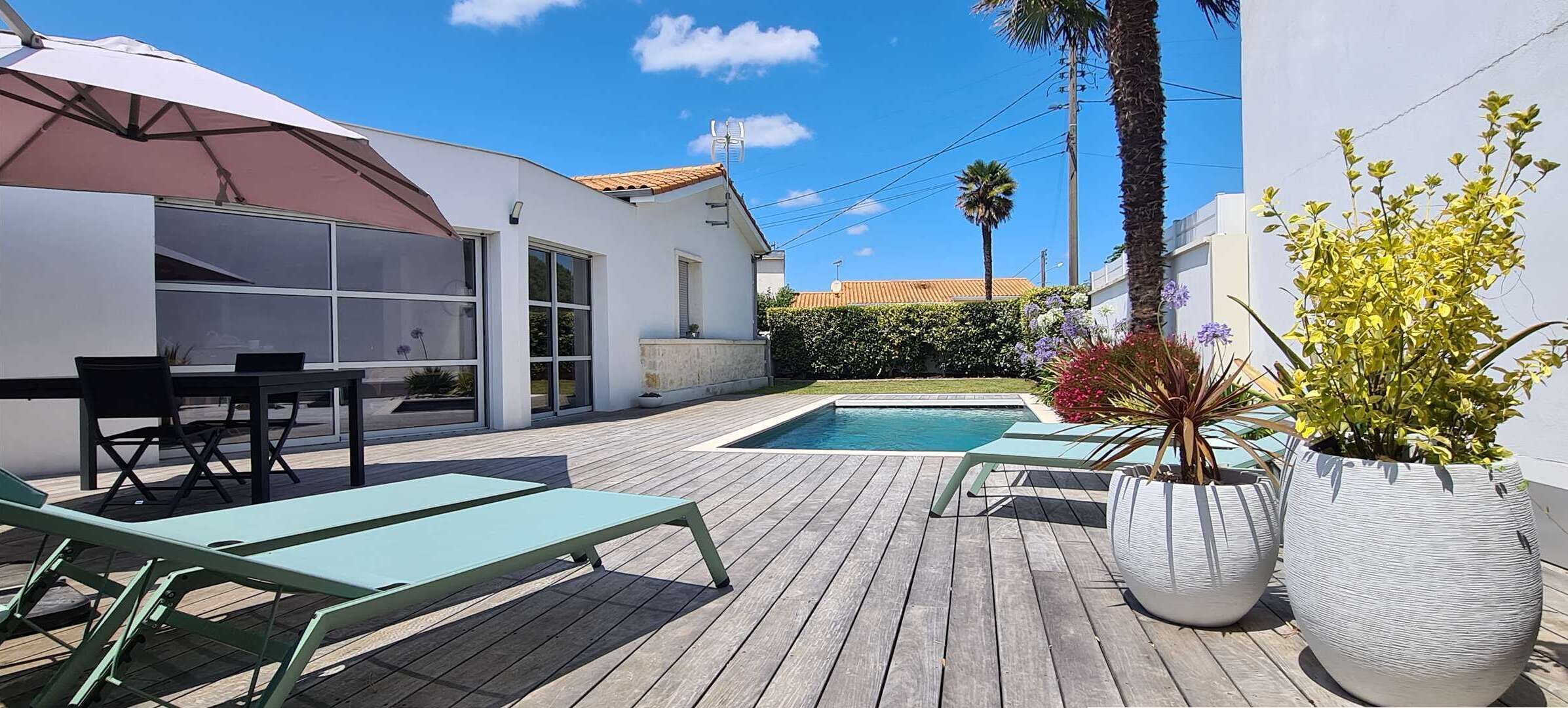 A wooden deck with lounge chairs, a swimming pool, and potted plants.